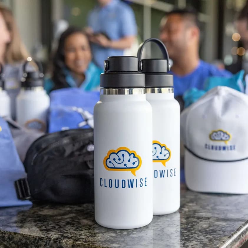 Custom branded water bottles and hats with the Cloudwise logo displayed on a table at a company event.