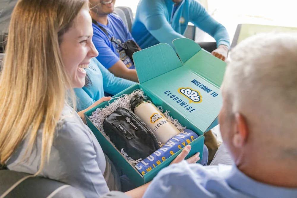 Smiling employee opening a custom Cloudwise welcome box containing branded apparel, water bottle, and accessories.
