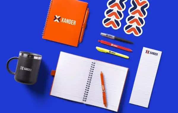 Custom branded office supplies including notebooks, pens, mug, and stickers with the Xander logo.